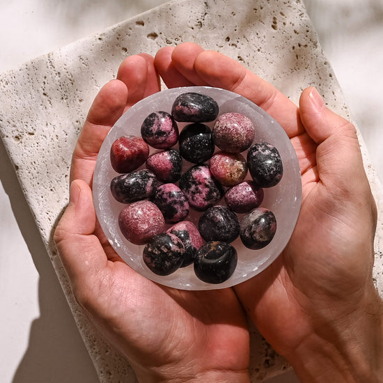 Hands holding Selenite bowl full of Rhodonite Tumbled Stones 